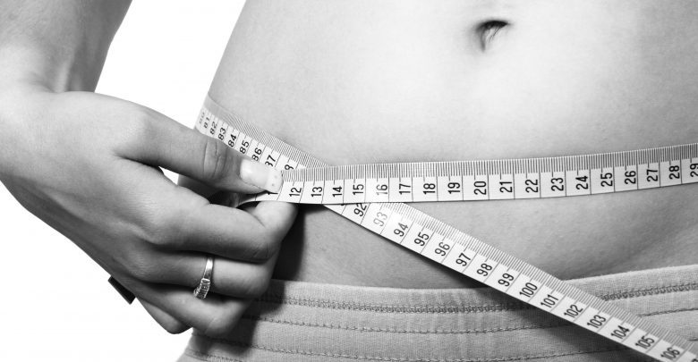 An image showing a fit woman measuring her waist
